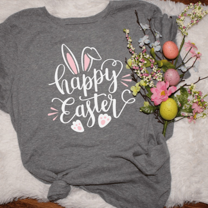 gray women's Happy Easter shirt with bunny ears and paw prints design beside pastel Easter eggs and spring flowers