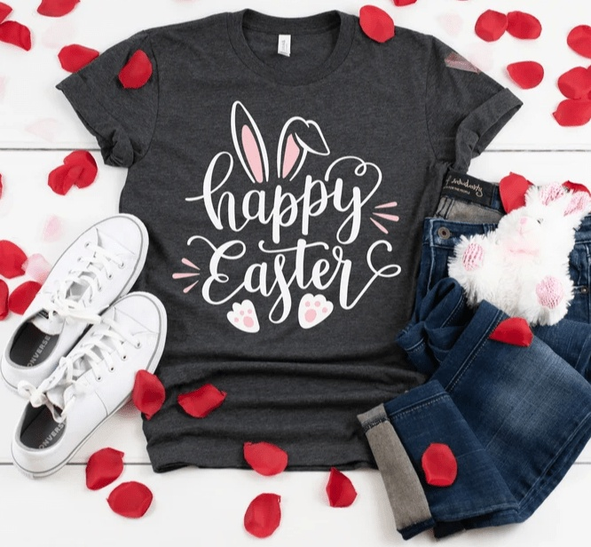Women's dark gray Happy Easter shirt with bunny ears and paws design, paired with white sneakers and blue jeans, surrounded by red rose petals.