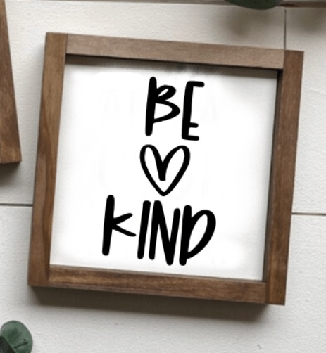 Handmade "Be Kind" sign with natural wood frame and black lettering on a white background.
