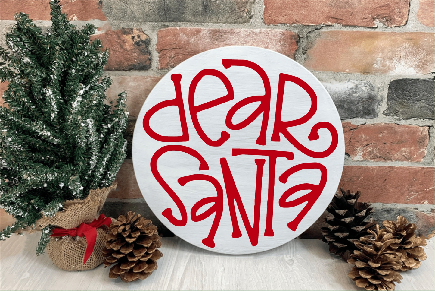"Dear Santa" wood sign with red lettering on a white background, displayed with pine cones and a decorative plant.