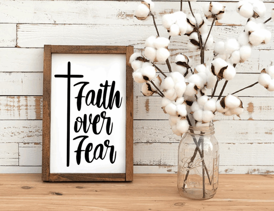Rustic wood sign with "Faith over Fear" lettering and cross design, framed with stained wood, beside cotton stems in a jar.