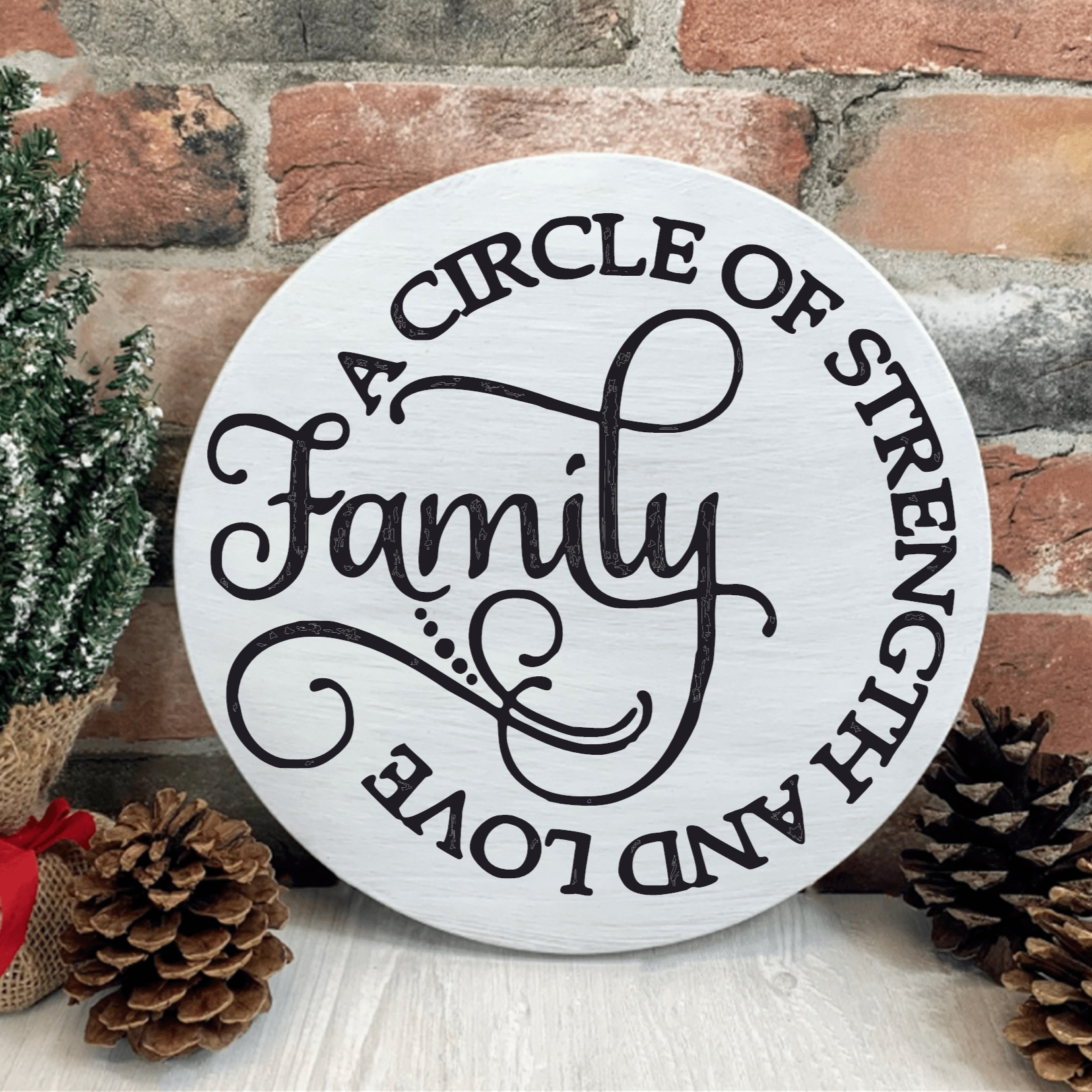 Handcrafted round wooden family sign reading "A Circle of Strength and Love," displayed on a table with pinecones and greenery.