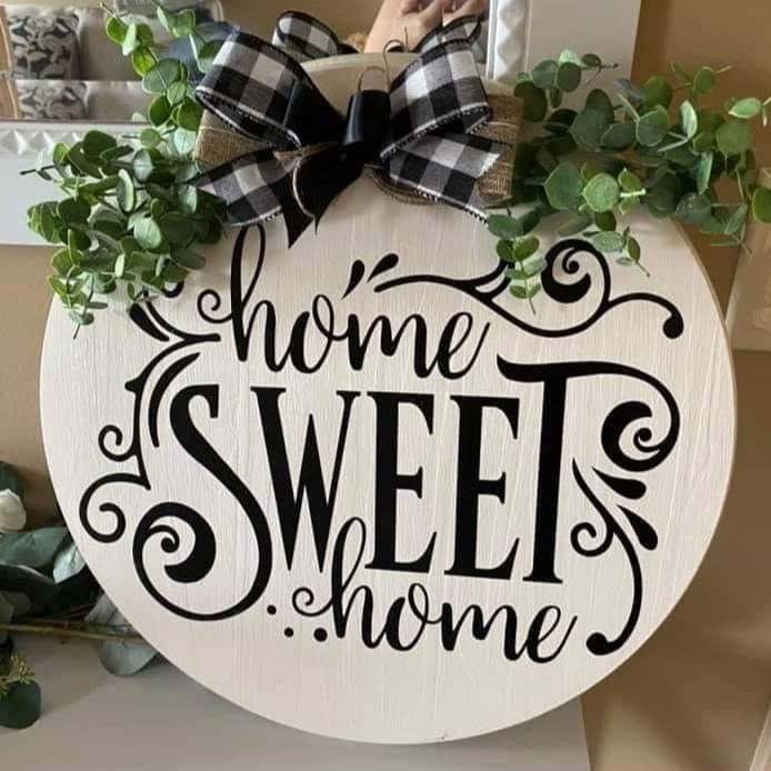 Round wood sign with "Home Sweet Home" text, adorned with a plaid ribbon and greenery.
