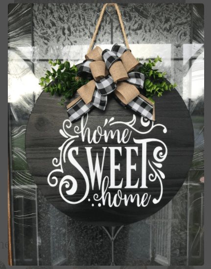 Round wooden "Home Sweet Home" sign with greenery and ribbon, hanging on a door.