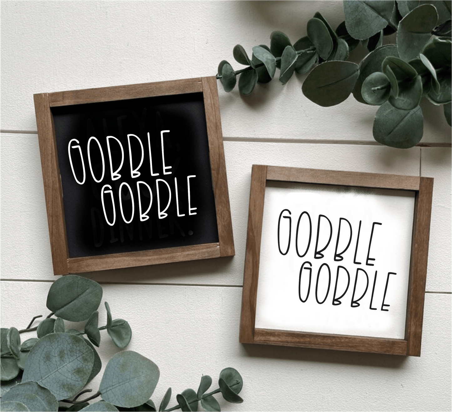 Handcrafted Gobble Gobble wood signs with black and white backgrounds, framed in stained wood, surrounded by green leaves.