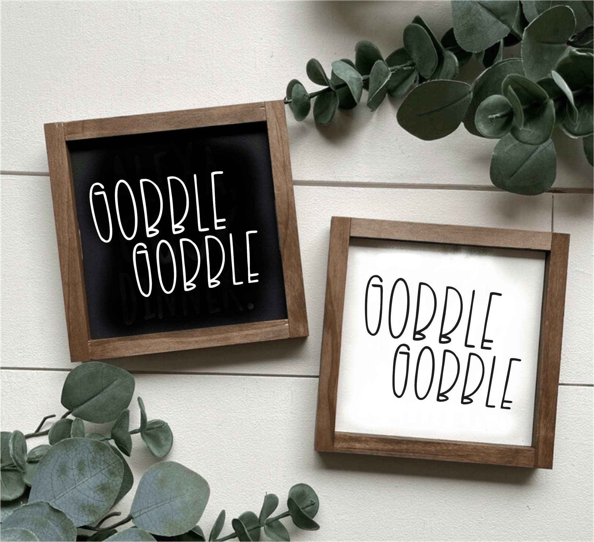 Handcrafted Gobble Gobble wood signs with black and white backgrounds, framed in stained wood, surrounded by green leaves.