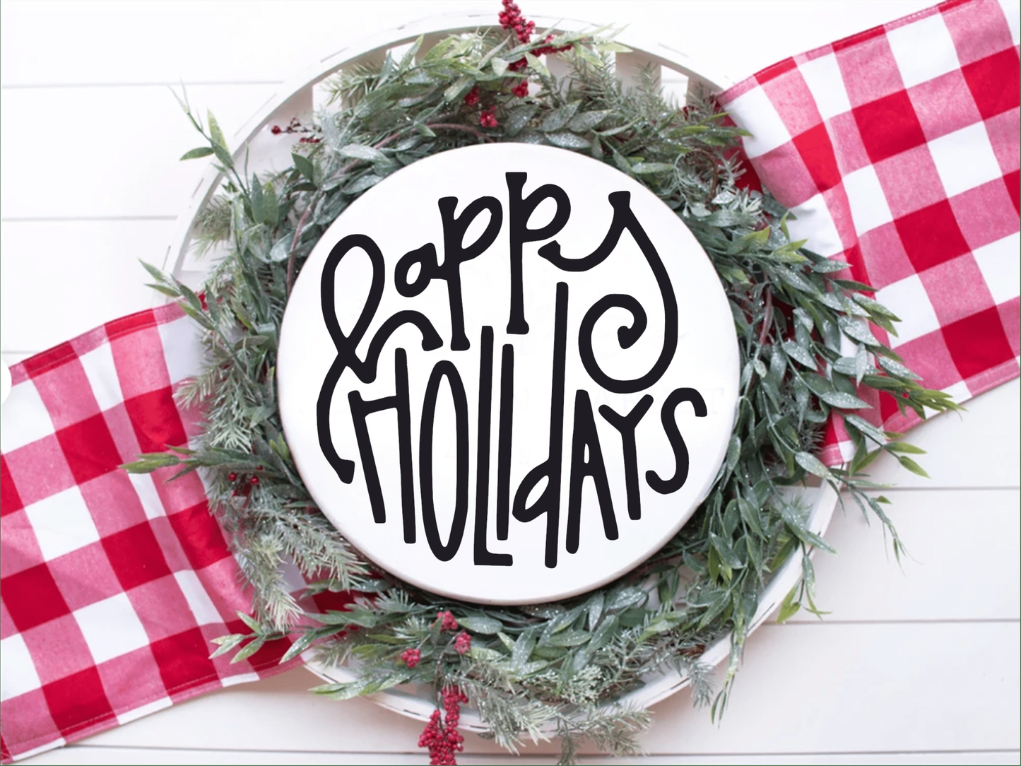 Round "Happy Holidays" wood sign with black lettering on a white background, accented with festive greens and red plaid ribbon.