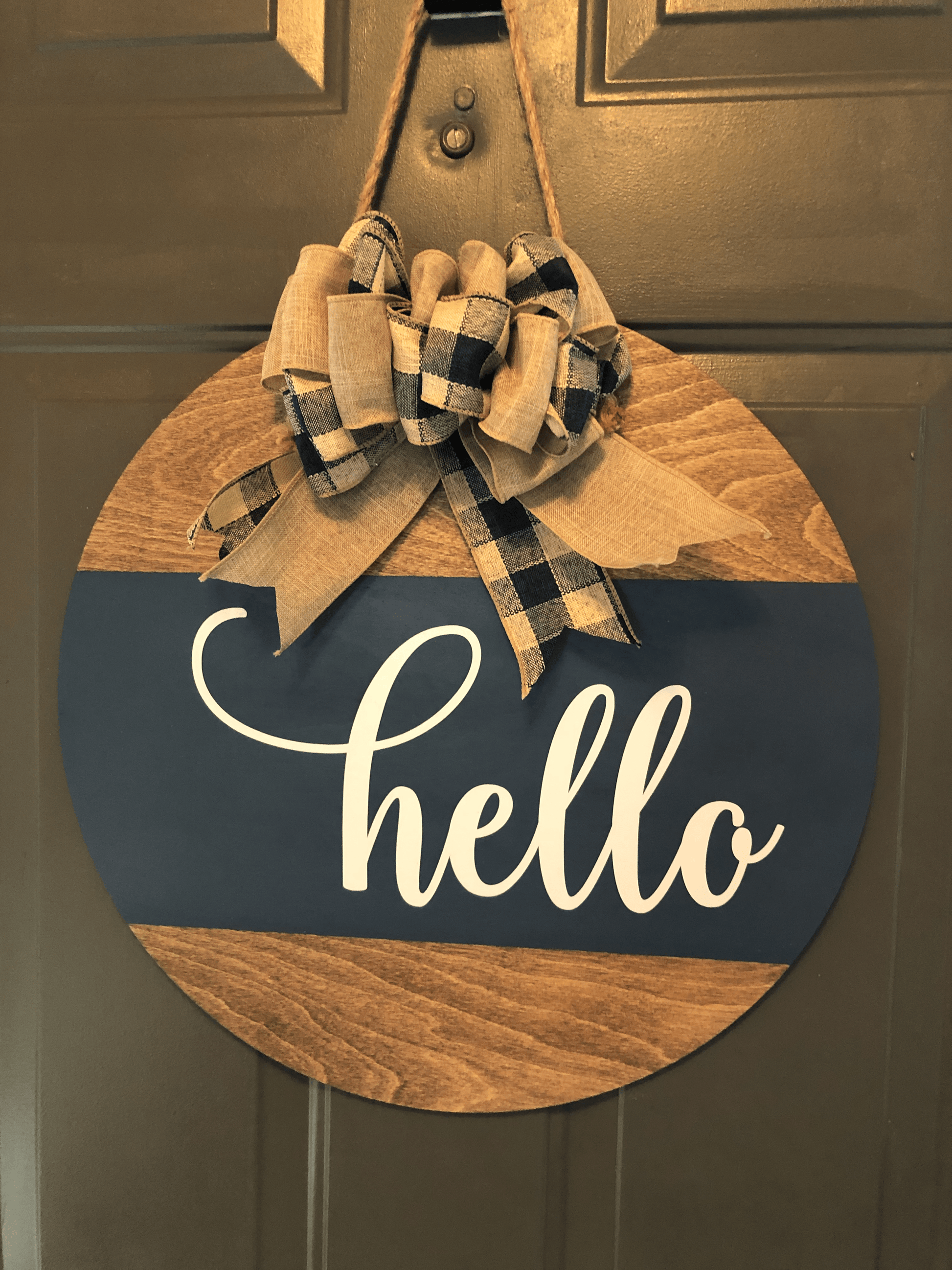 Handcrafted round wood door sign with "hello" text, adorned with a ribbon.