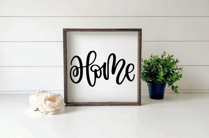 Handcrafted wood sign with "Home" in black script on a white background, framed in dark wood.