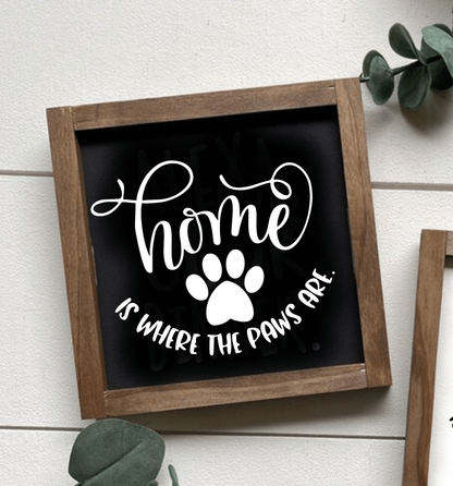 Handcrafted wood sign with "Home is where the paws are" in white lettering on a black background, framed in stained wood.