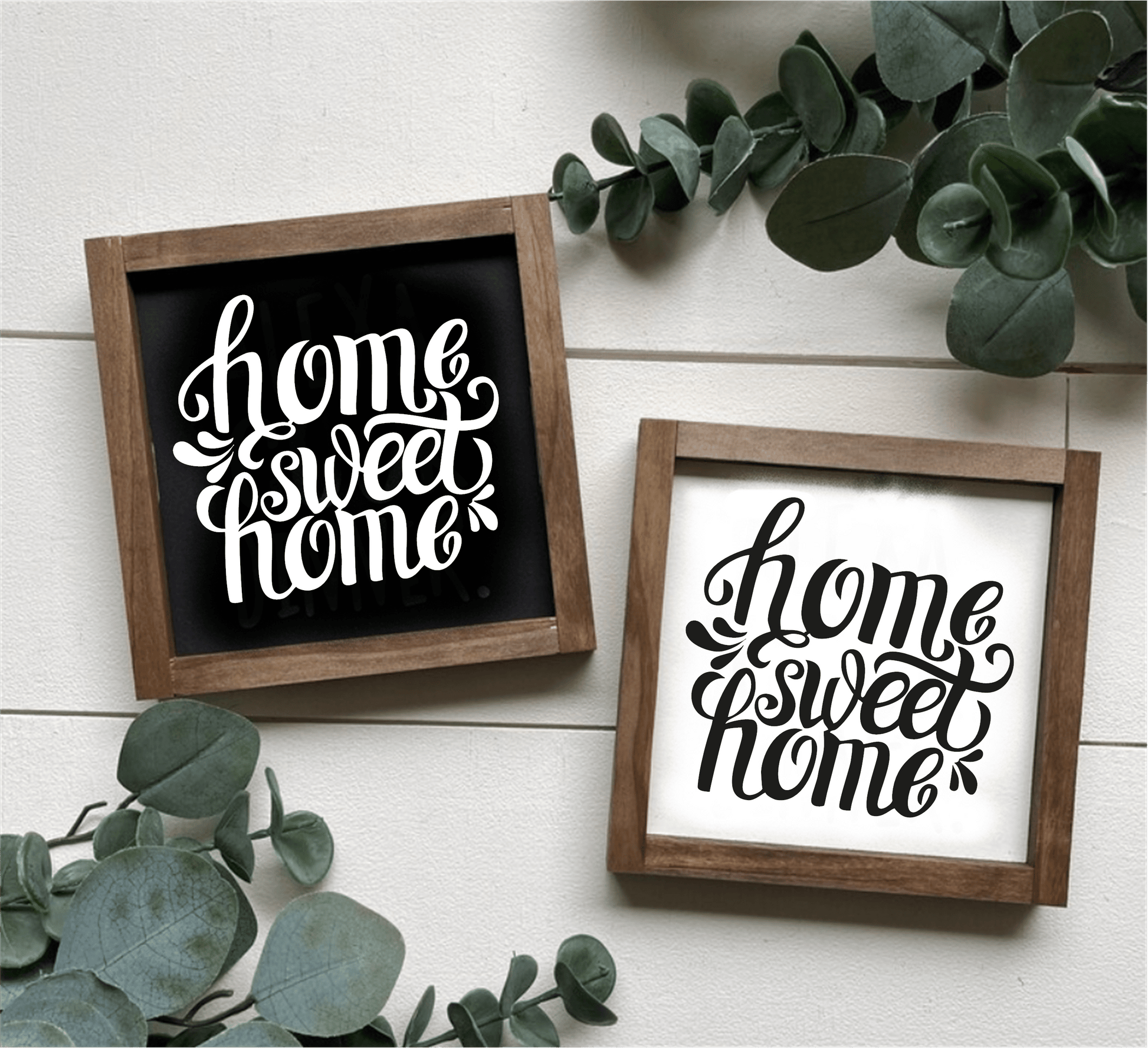 Handcrafted "Home Sweet Home" framed wood signs with white and black backgrounds and contrasting lettering, surrounded by greenery.