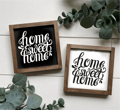 Handcrafted "Home Sweet Home" framed wood signs with white and black backgrounds and contrasting lettering, surrounded by greenery.