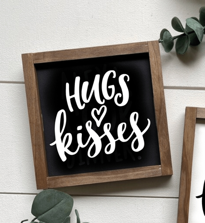 Handcrafted "Hugs and Kisses" wood sign with black background and white lettering, framed in natural wood.