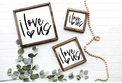 Handcrafted "I Love Us" wood signs with rustic frames in various sizes, featuring black lettering on a white background, styled with greenery and decorative beads.
