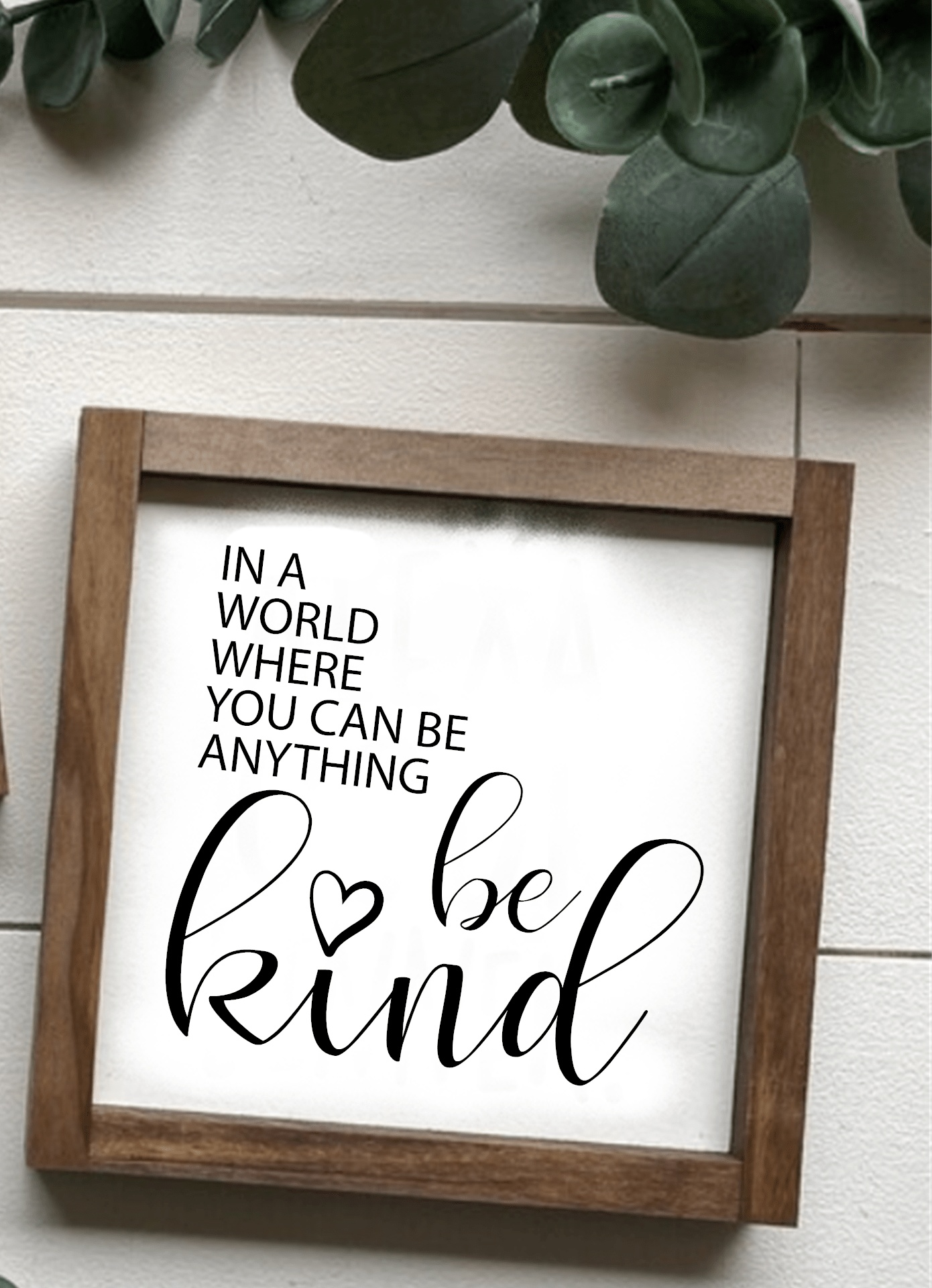Framed wood sign with "In a World where you can be Anything Be Kind" text on white background.