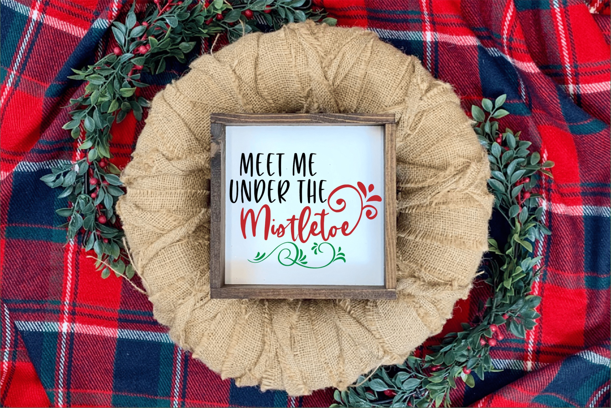 Meet Me Under the Mistletoe wood framed sign on plaid background.