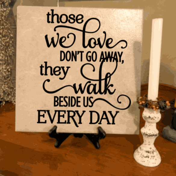 Memorial ceramic tile with vinyl lettering, "Those We Love Don't Go Away," displayed on a stand.