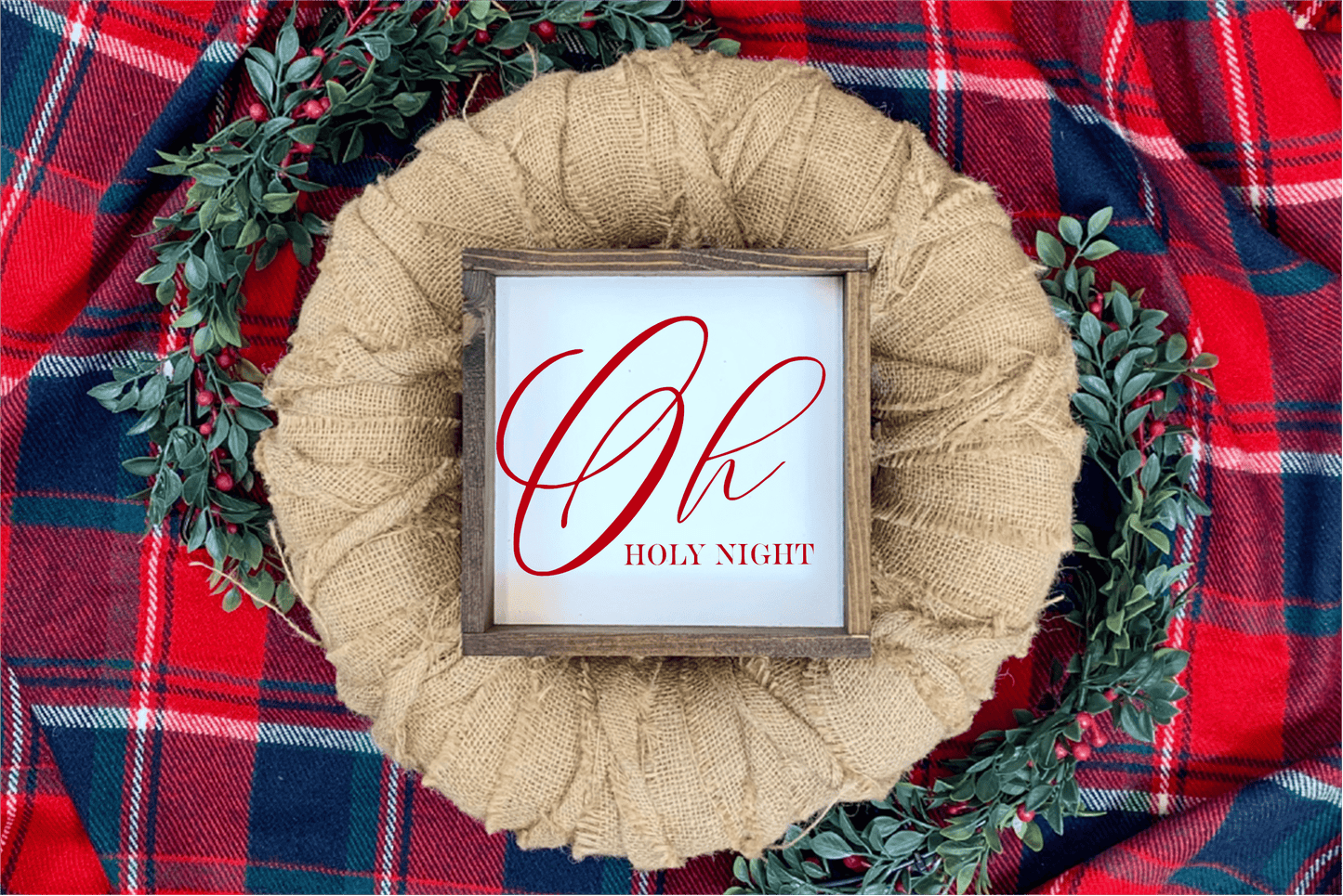 Oh Holy Night Christmas wood sign with red lettering and rustic frame on plaid background with greenery.
