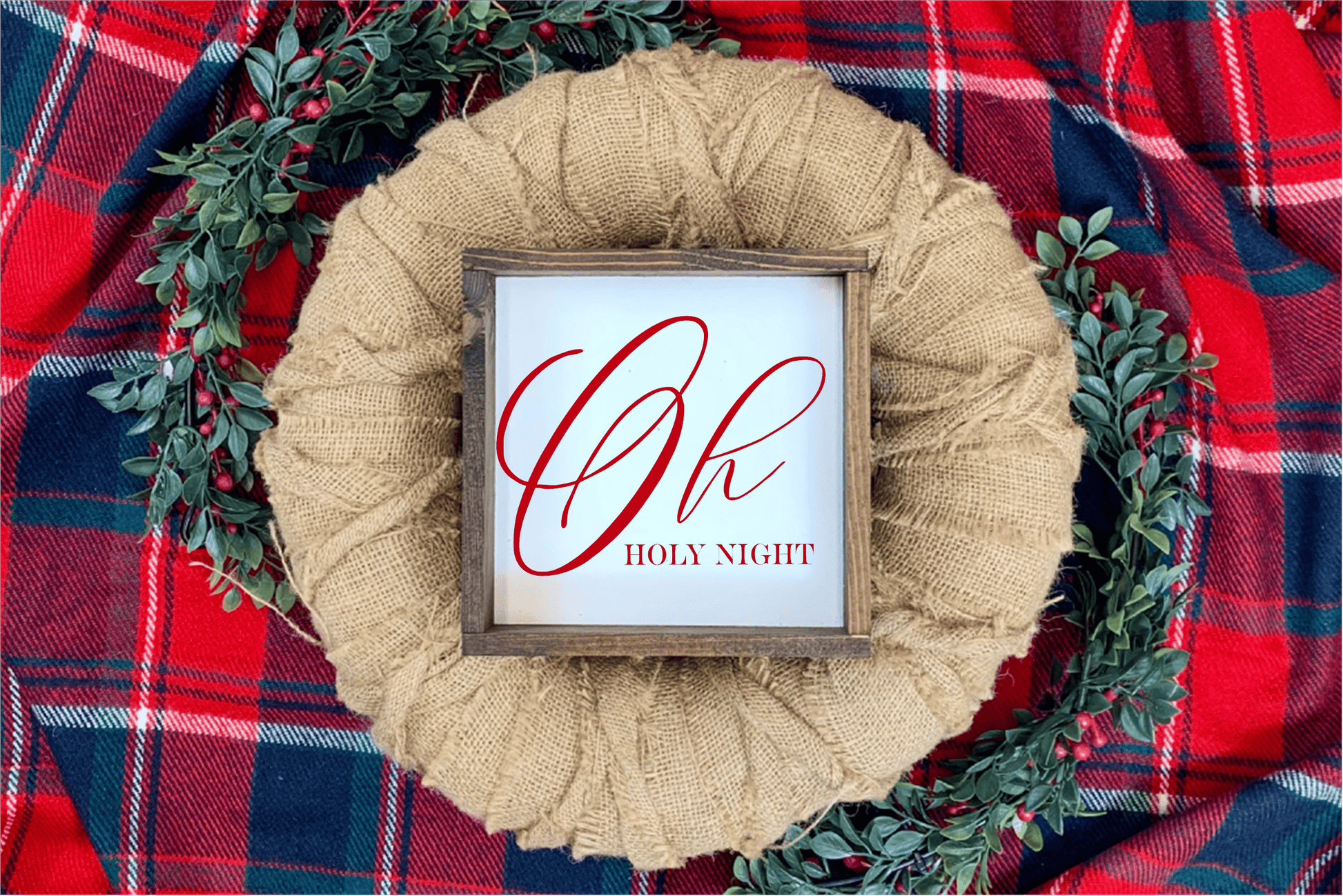 Oh Holy Night Christmas wood sign with red lettering and rustic frame on plaid background with greenery.