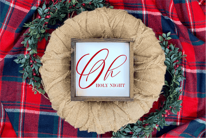 Oh Holy Night Christmas wood sign with red lettering and rustic frame on plaid background with greenery.