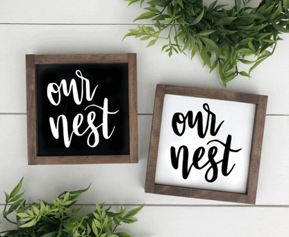 Handcrafted "Our Nest" wood sign with black and white options, framed and adorned with greenery, perfect for home decor.