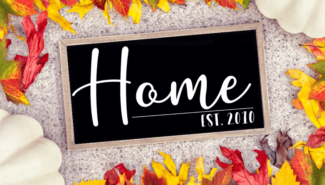 Rustic farmhouse wood sign with "Home Est. 2010" customizable design, black background, surrounded by autumn leaves.