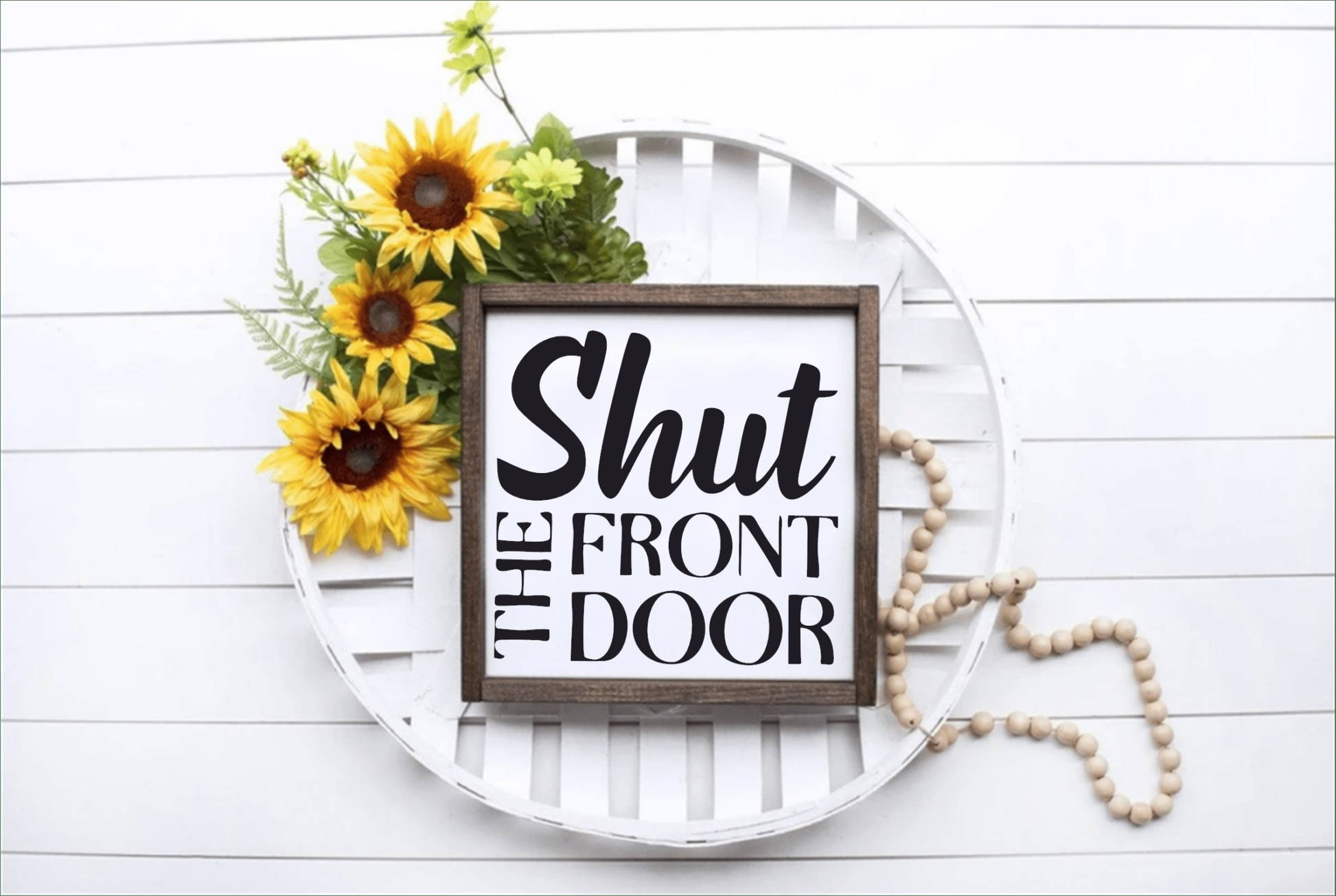 Handcrafted wood sign with "Shut the Front Door" text, framed and placed on a decorative tray with sunflowers.
