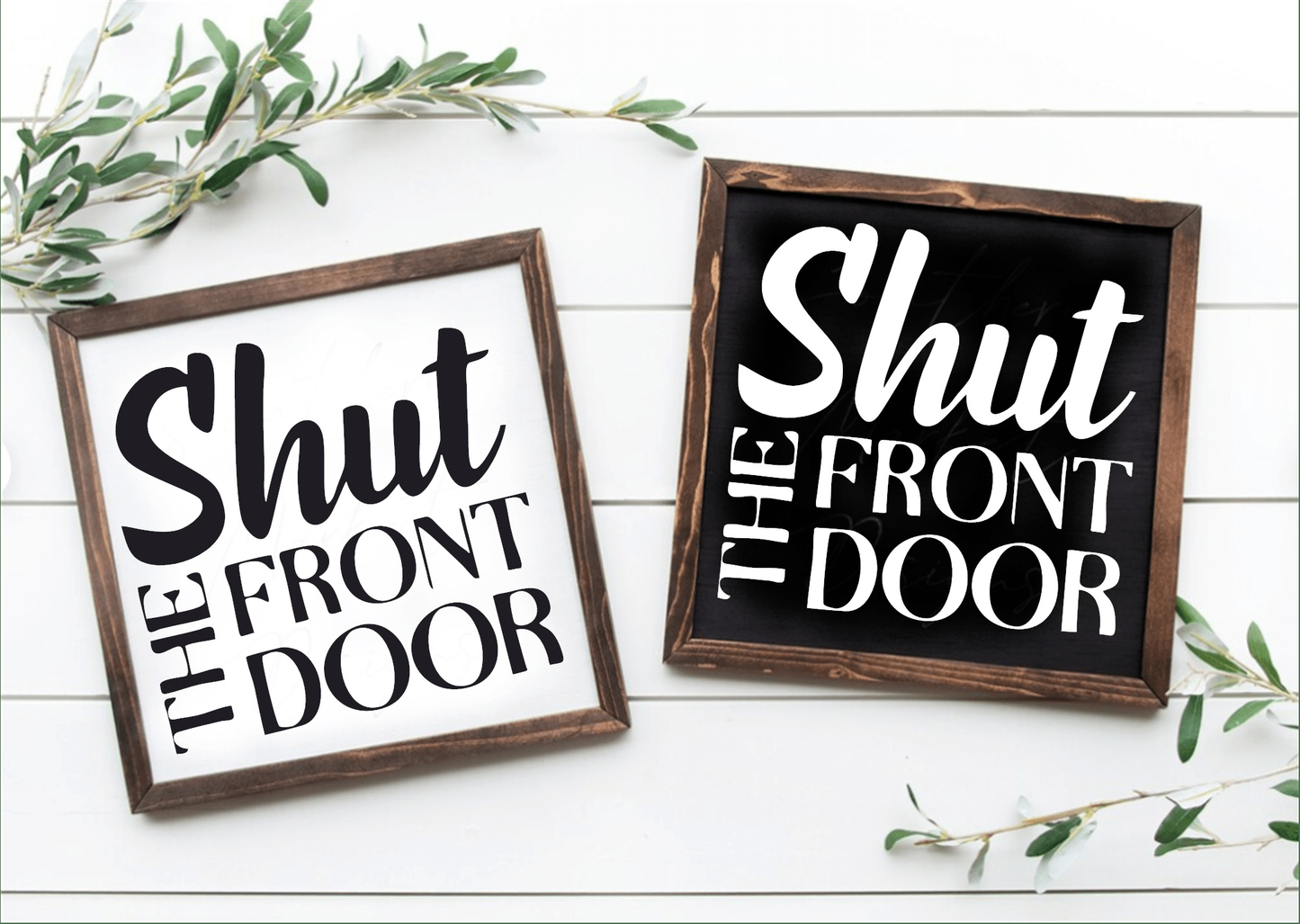 Handcrafted "Shut the Front Door" framed wood signs, black and white backgrounds with contrasting lettering, showcased on a white surface with greenery accents.