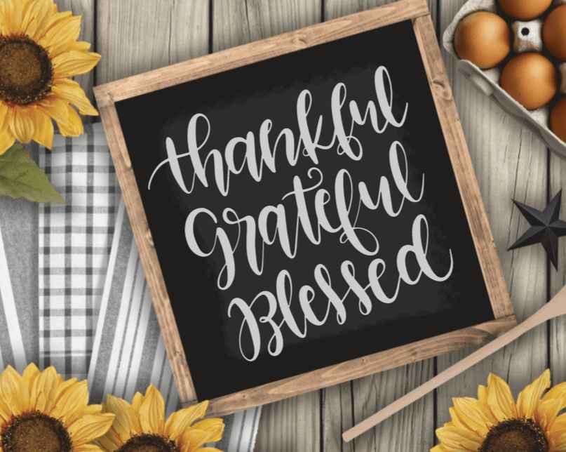 Thankful Grateful Blessed wood sign with black background and white lettering, surrounded by sunflowers.
