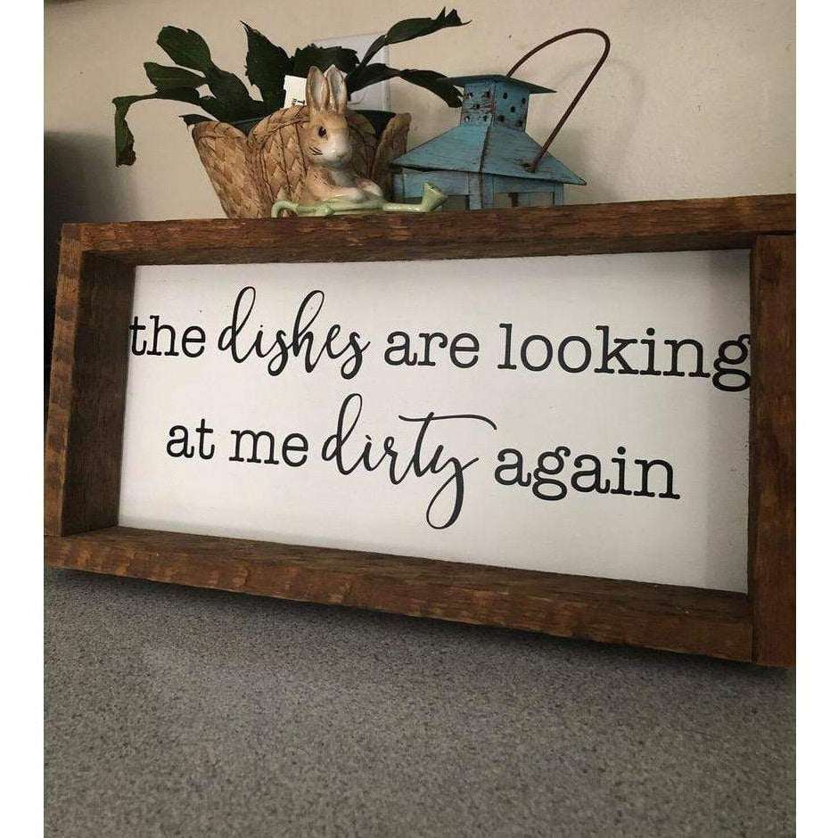 Rustic kitchen wood sign with the phrase "The Dishes are Looking at me Dirty Again" in black lettering on a white background, framed with pine wood.