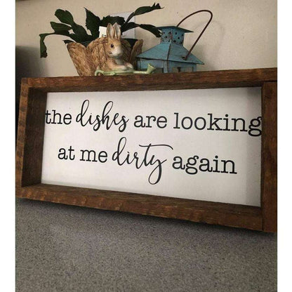 Rustic kitchen wood sign with the phrase "The Dishes are Looking at me Dirty Again" in black lettering on a white background, framed with pine wood.