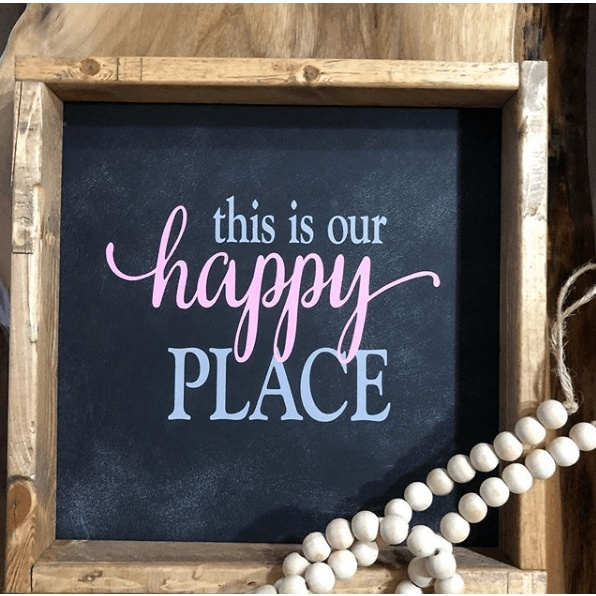 Wood framed sign with "This is Our Happy Place" in pink and white lettering on a black background.