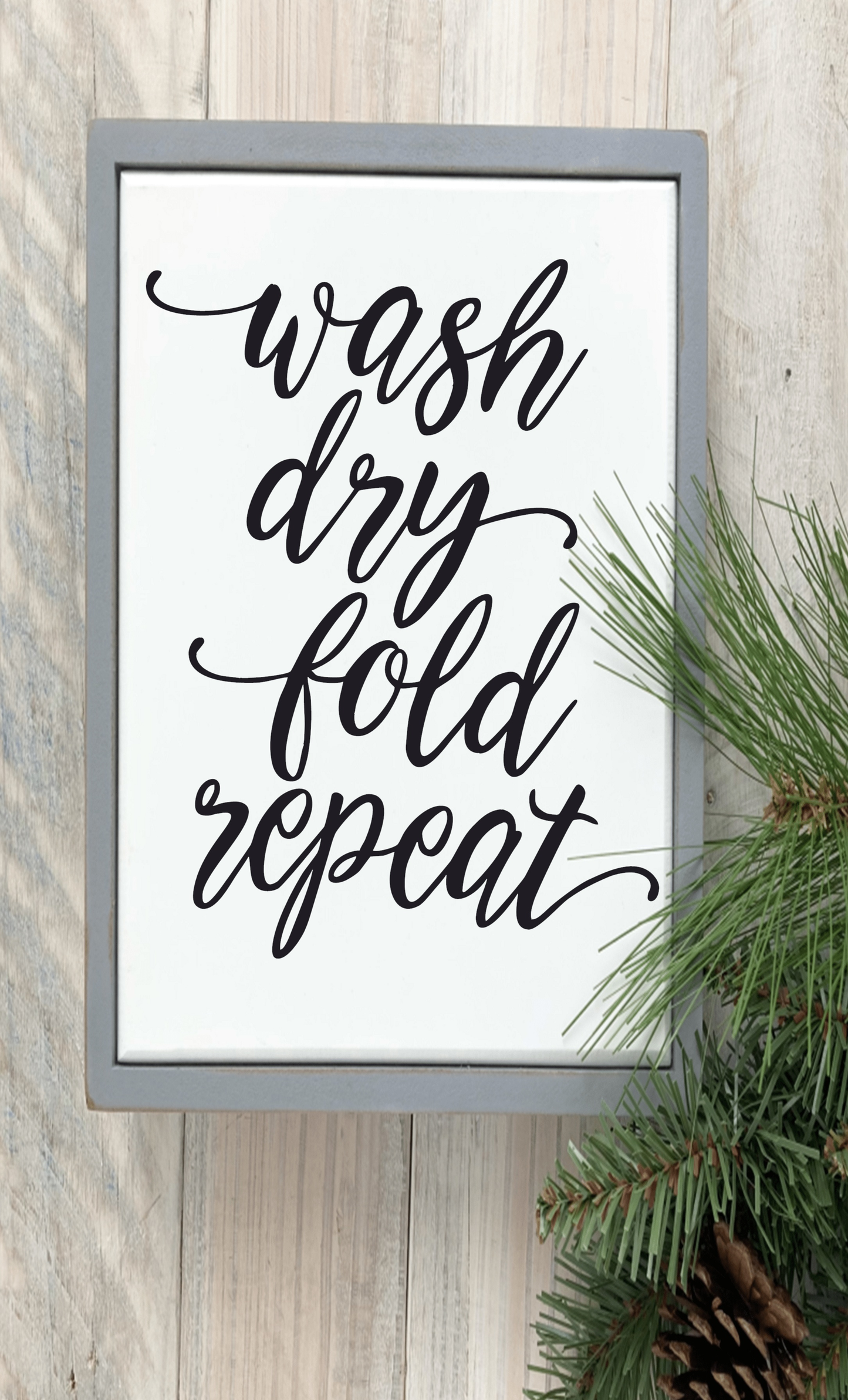 Handcrafted "Wash Dry Fold Repeat" wood sign with black lettering on a white background, framed in gray.