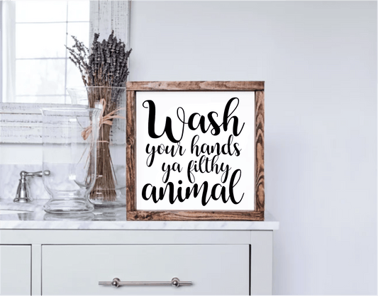 Hands Ya Filthy Animal Framed Wood Sign with black lettering on white background in rustic wooden frame on bathroom countertop