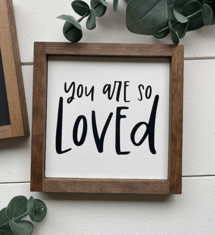 Hand-painted "You Are Loved" wooden sign with stained frame and white background featuring black lettering.