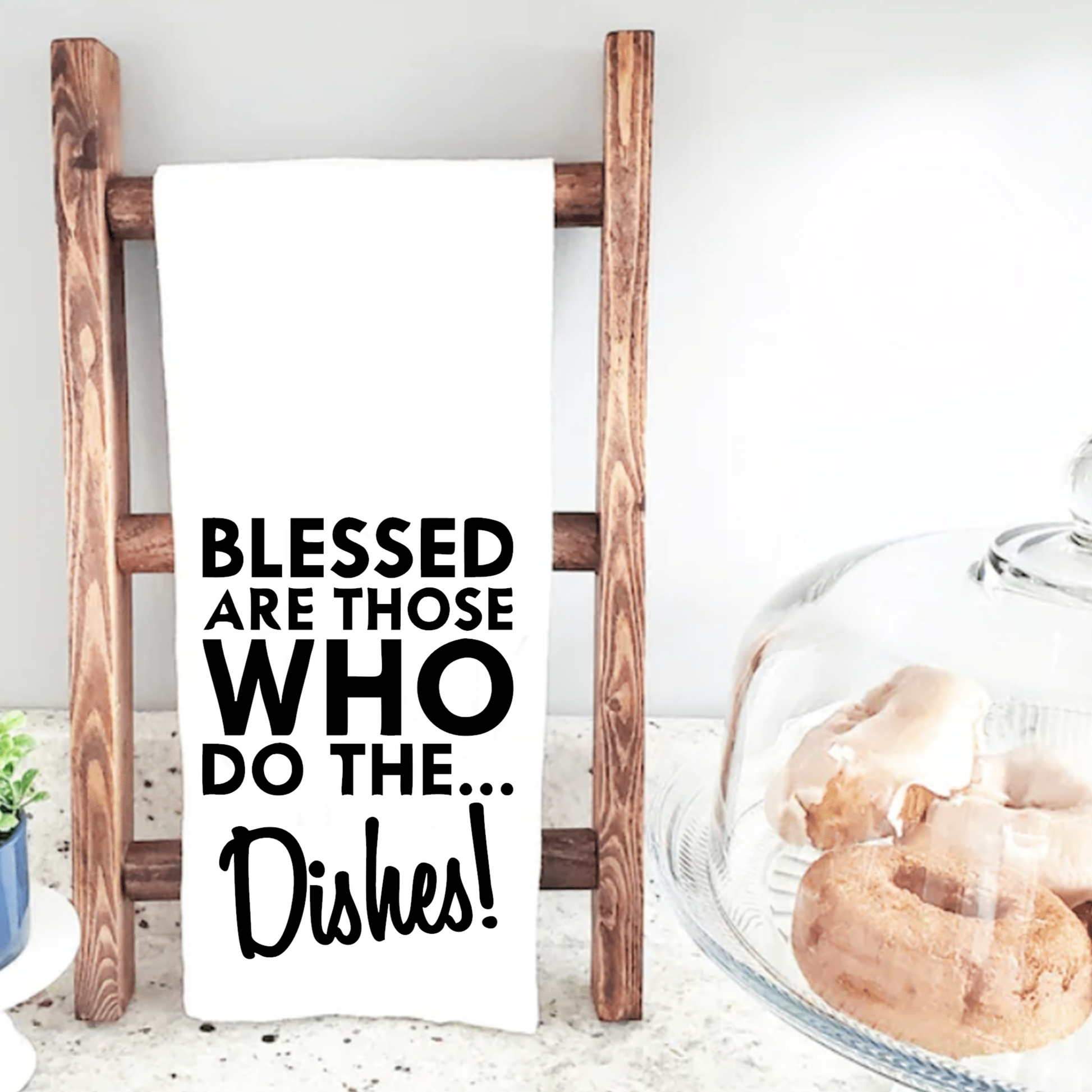Tea towel with "Blessed are Those Who Do The Dishes" message on wooden ladder, kitchen decor.