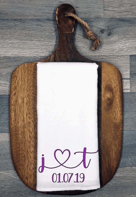 Personalized initials and heart tea towel on wooden board.