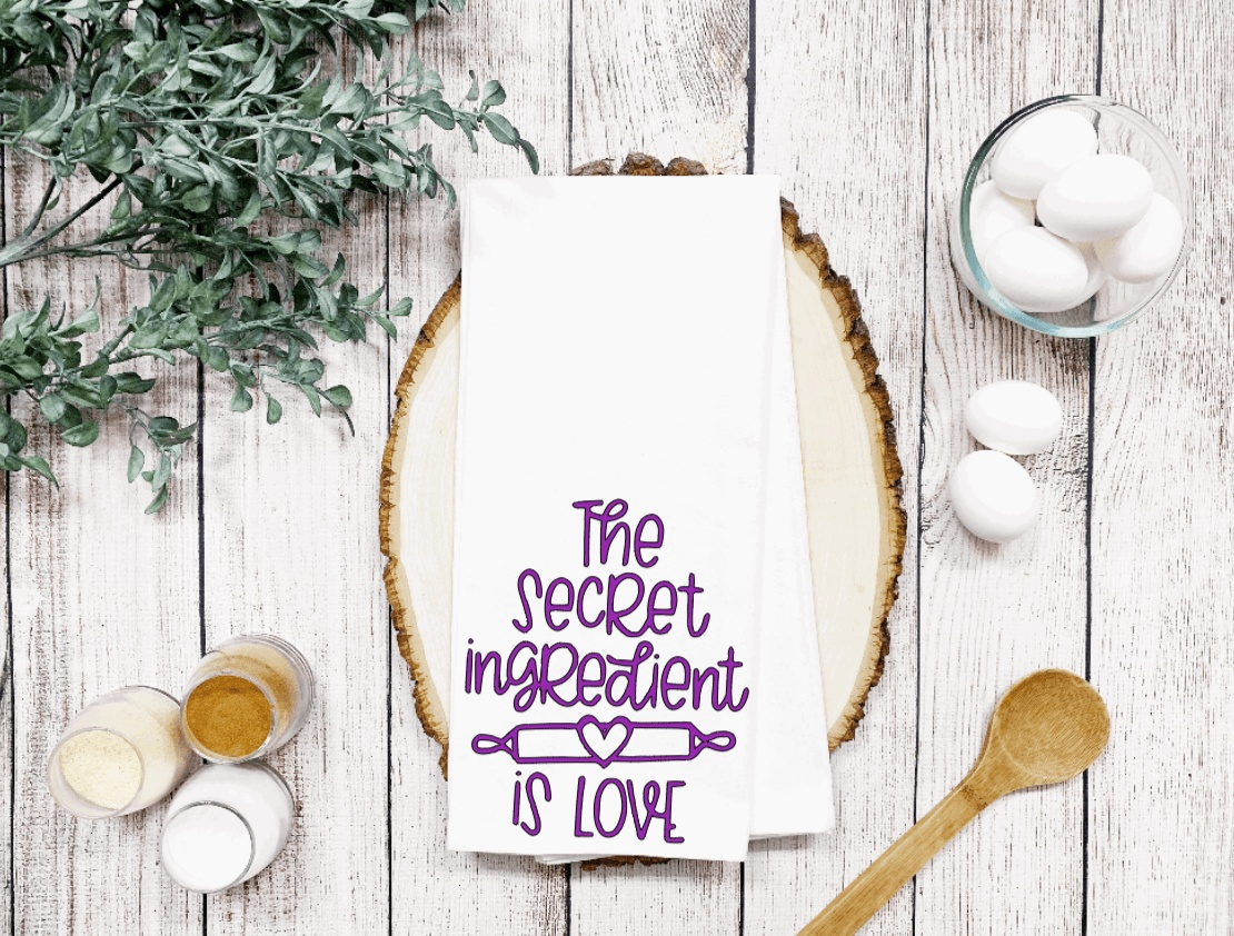 Waffle weave tea towel with "The Secret Ingredient is Love" design, perfect for kitchen decor and gifts.
