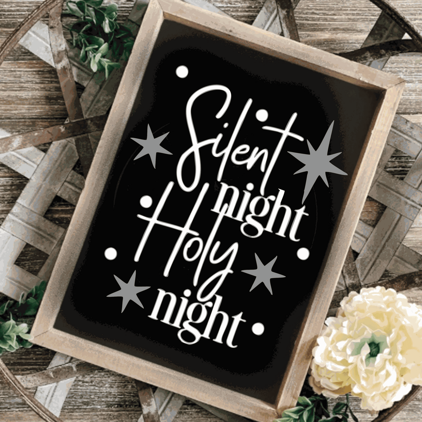 "Silent Night, Holy Night" framed wood sign with black background, white lettering, and silver stars on a rustic surface.
