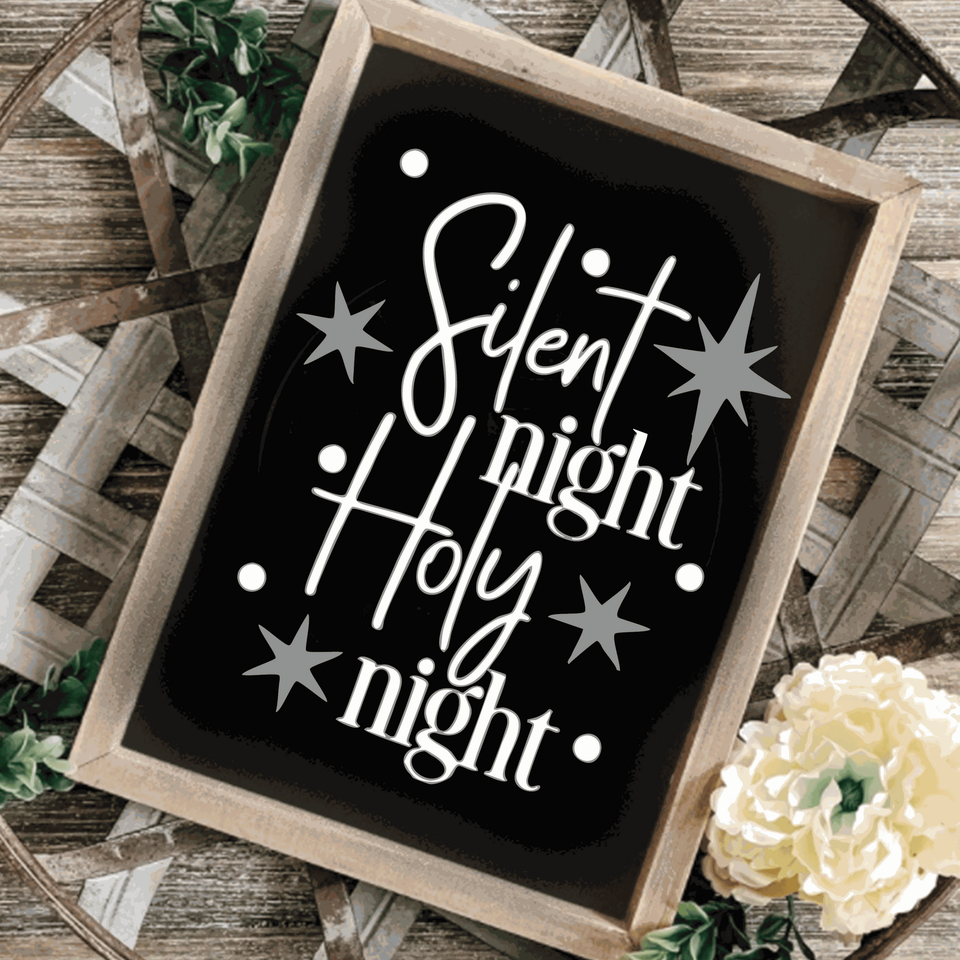 "Silent Night, Holy Night" framed wood sign with black background, white lettering, and silver stars on a rustic surface.